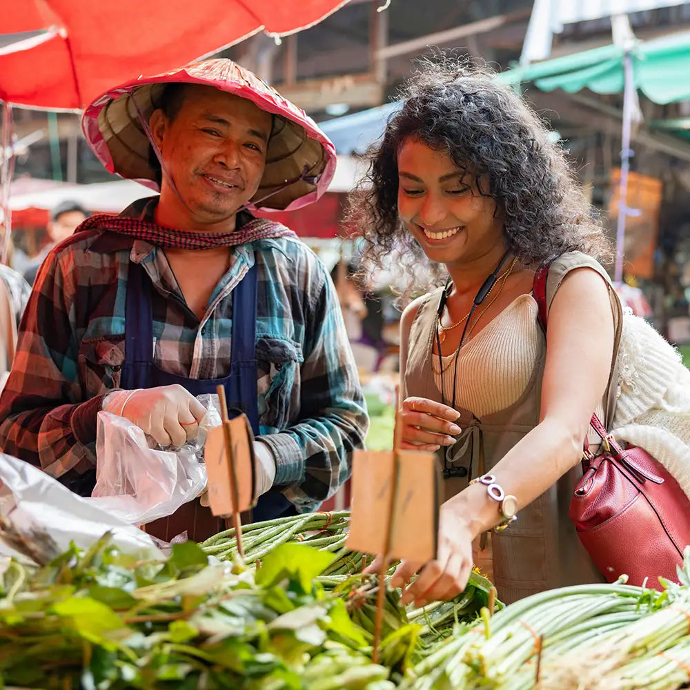 Woman shopping at a market with a vendor, surrounded by green vegetables.