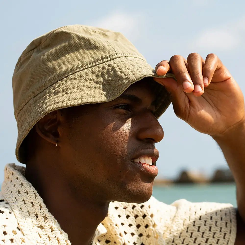 Man wearing a beige bucket hat with a blurred beach background