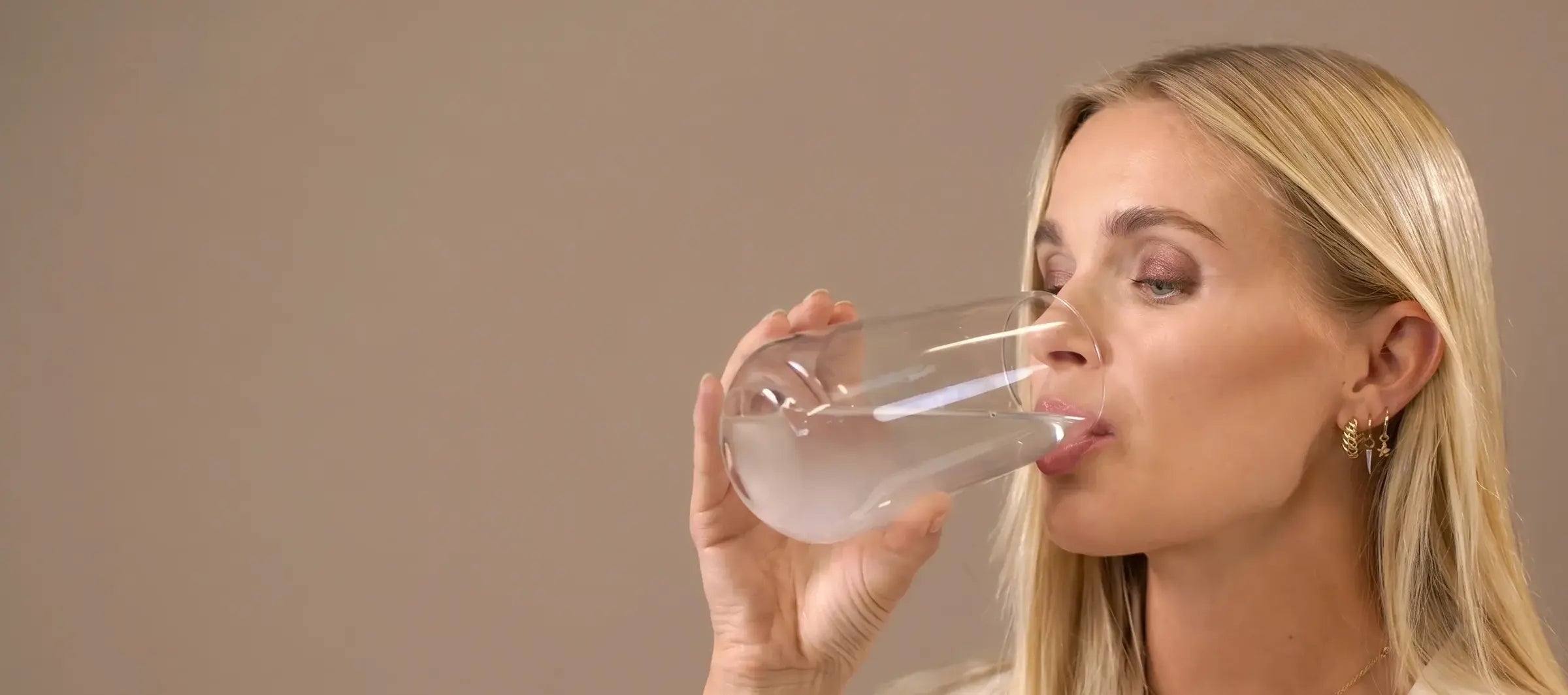 Woman drinking from a clear glass of Enterosgel mixed into water on a beige background
